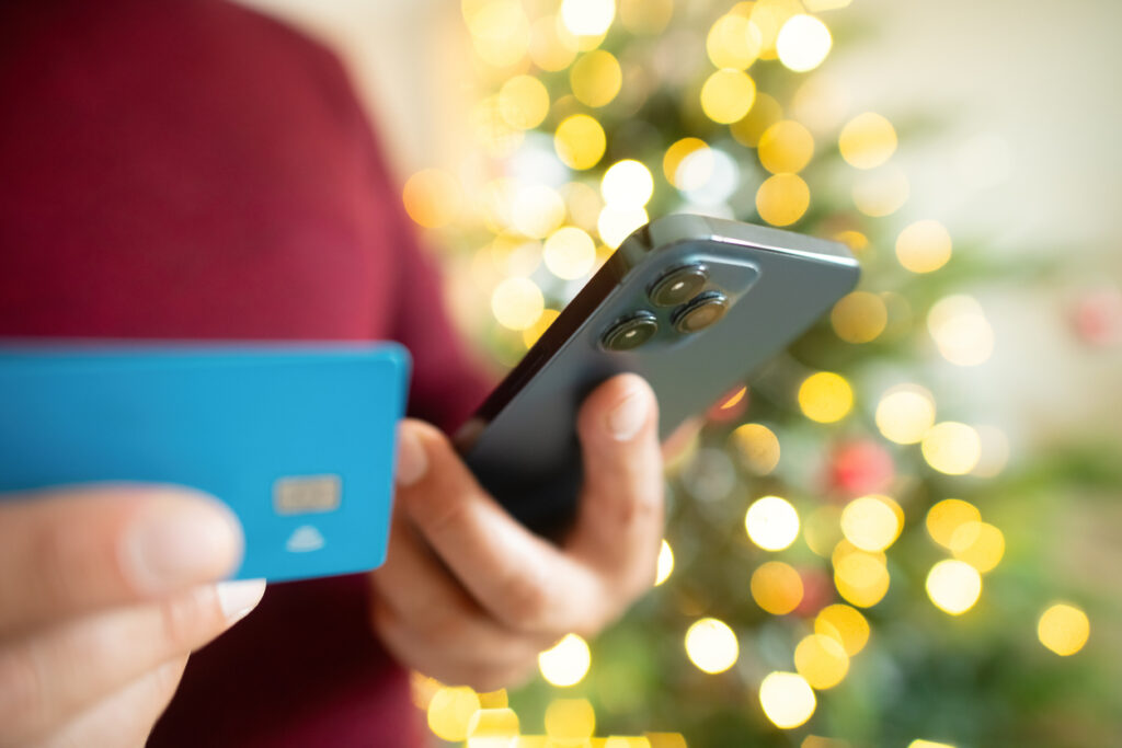 Man with smartphone and credit card near Christmas tree