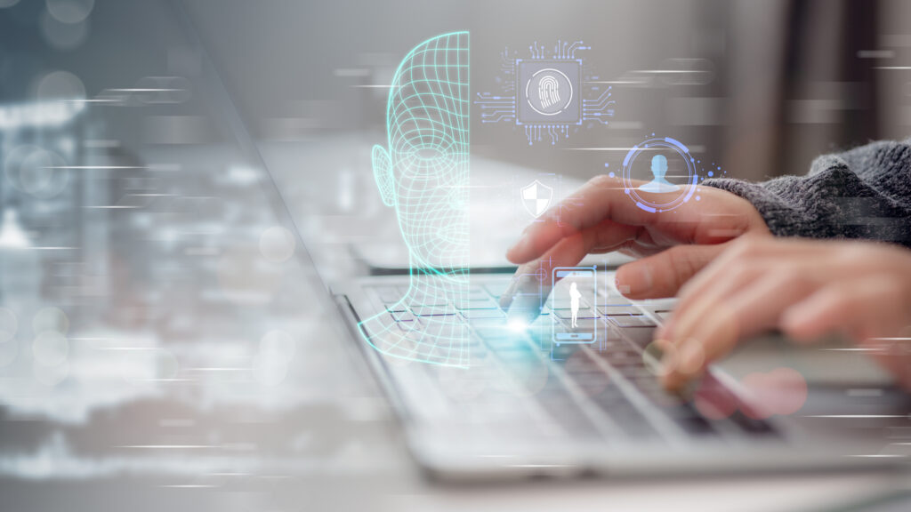 Hands typing on laptop with floating graphics of facial recognition and fingerprints.